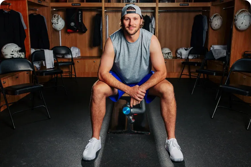 Pro football player running a Theragun over his legs between games